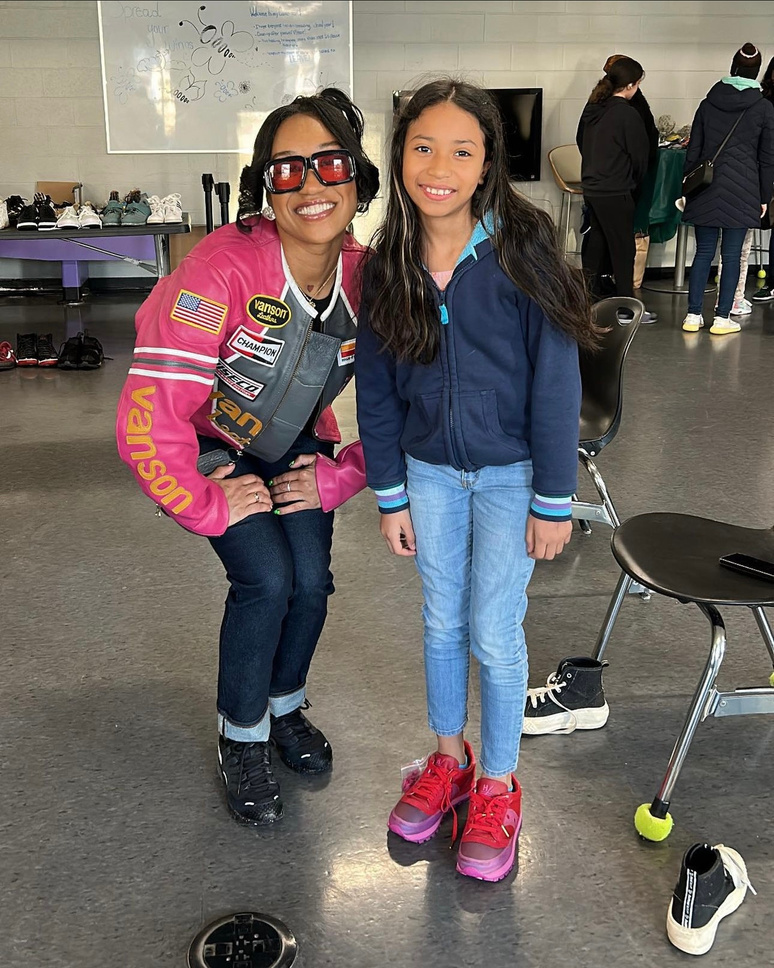 Dalisha Pinto crouching beside a girl wearing her new red sneakers at a giveaway.
