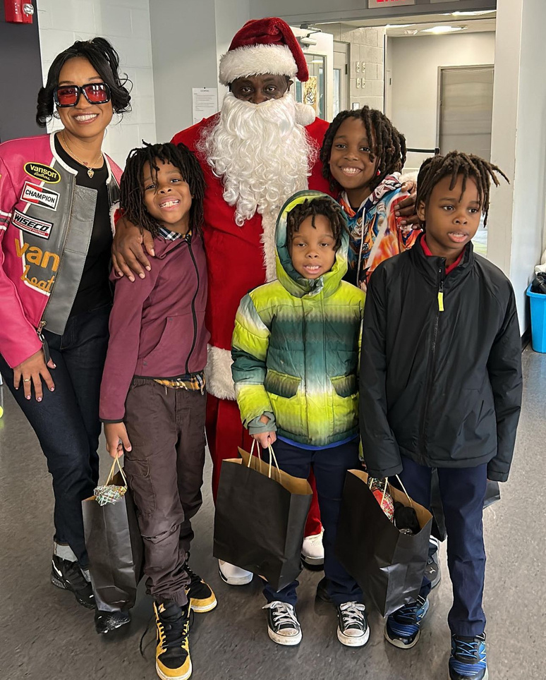 Dalisha Pinto and four boys standing with Santa at a giveaway, each child holding a gift bag.