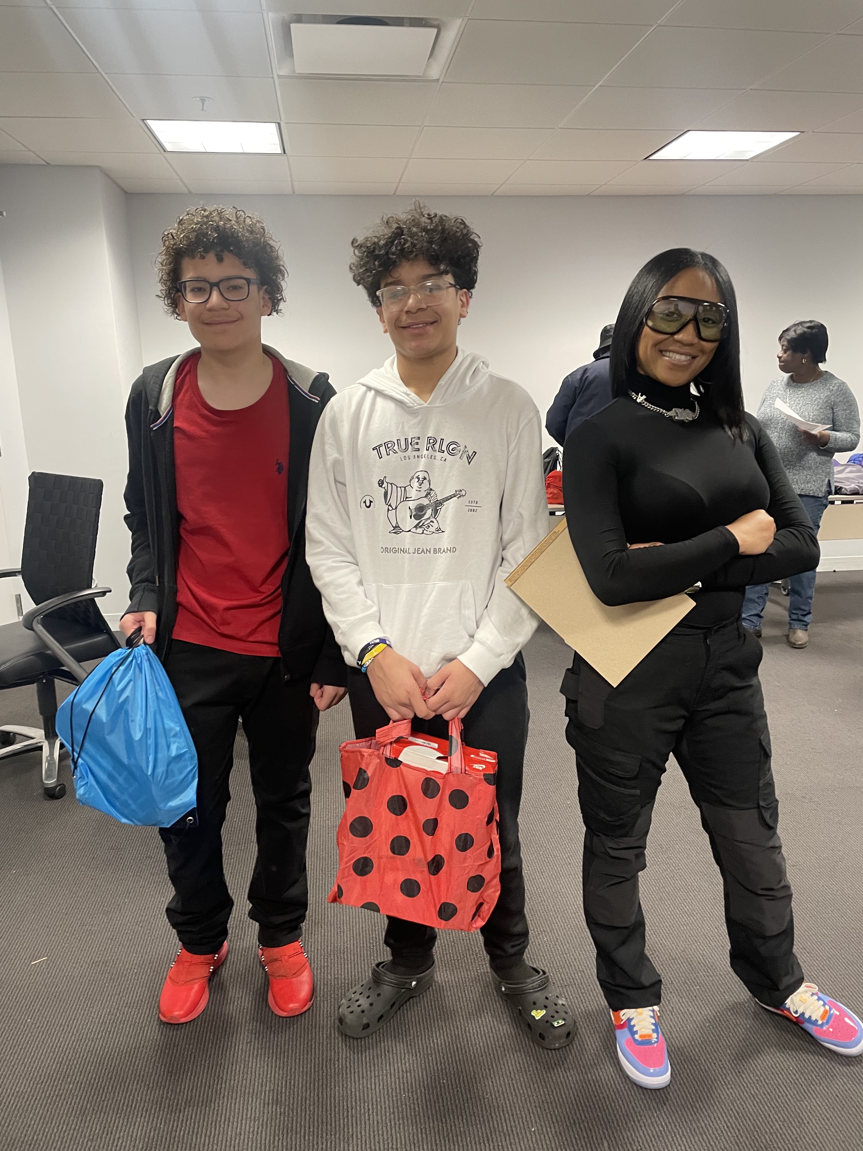 Two teenagers holding bags of donated sneakers, standing with Dalisha Pinto at a giveaway.