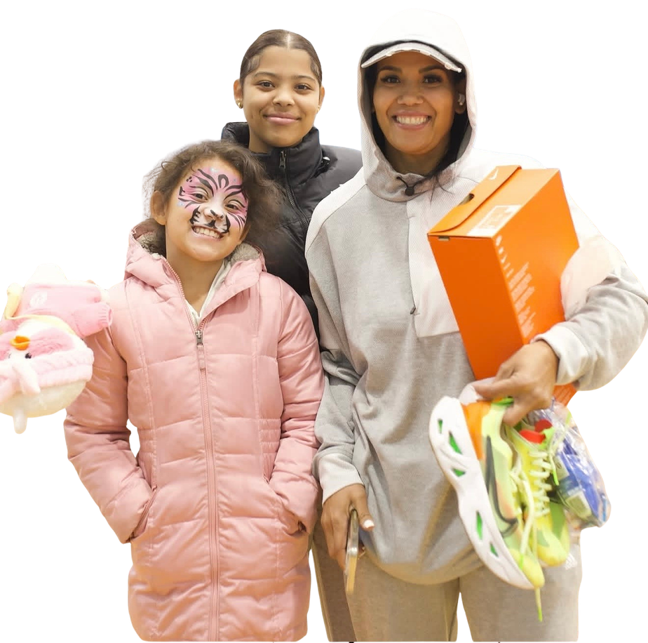A parent carrying an orange Nike shoebox and a pair of new sneakers, with two children beside her, one in tiger face paint.