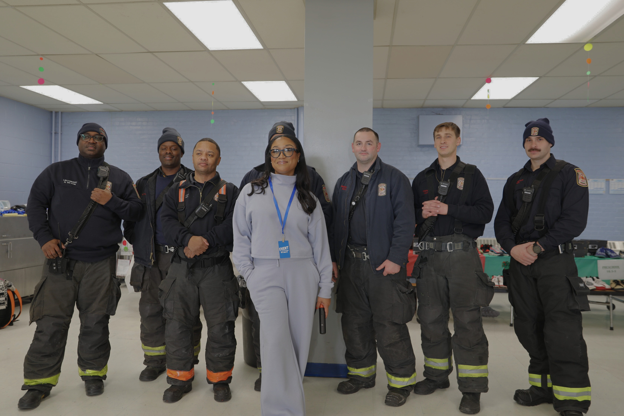 Dalisha Pinto standing with a group of firefighters at a giveaway, with tables of donated sneakers behind them.