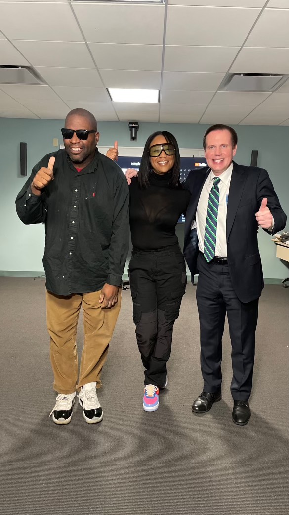 Dalisha Pinto standing between two partners at a meeting, all three giving a thumbs up.