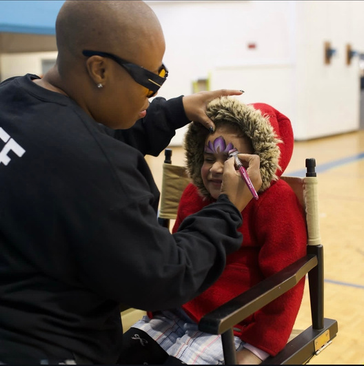 A volunteer painting a young child's face at a giveaway.